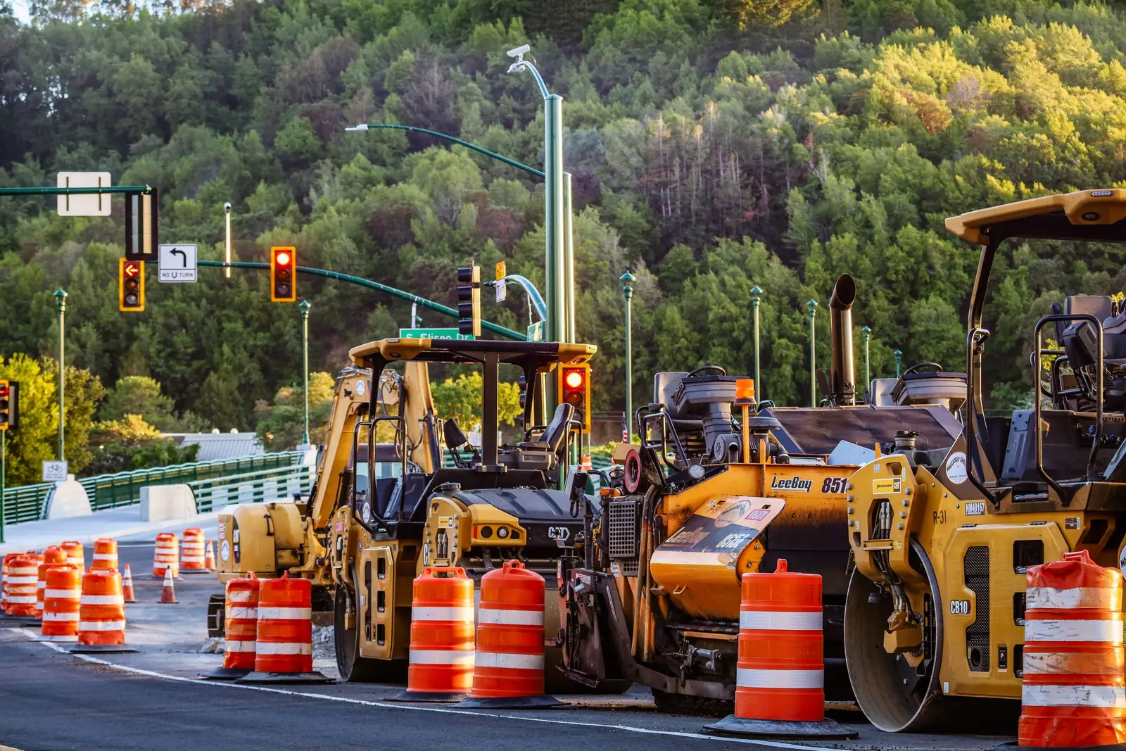 Two road rollers compacting a fresh lane inside a coned work zone.